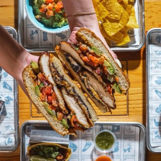 Hands holding a pressed sandwich over a table of shared plates.